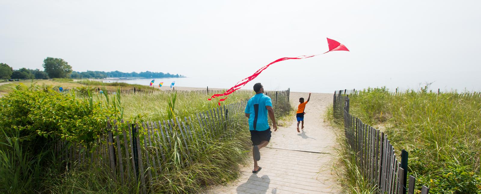 Father and son running toward water flying a kite on Sherwood Island