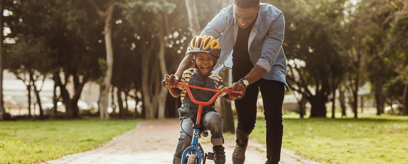 Father teaching son to ride his bike in state park