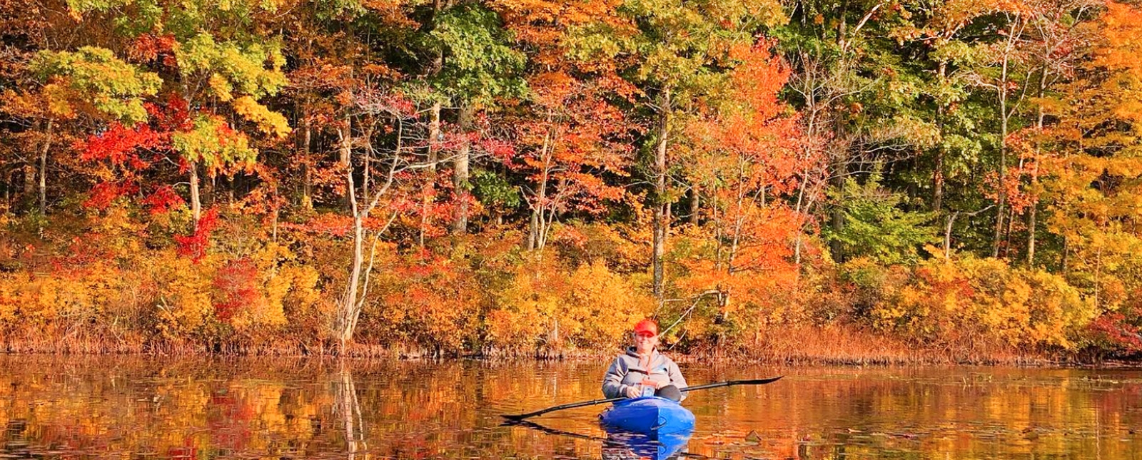 Una mujer navegando en kayak por un estanque rodeado de un vibrante follaje otoñal.