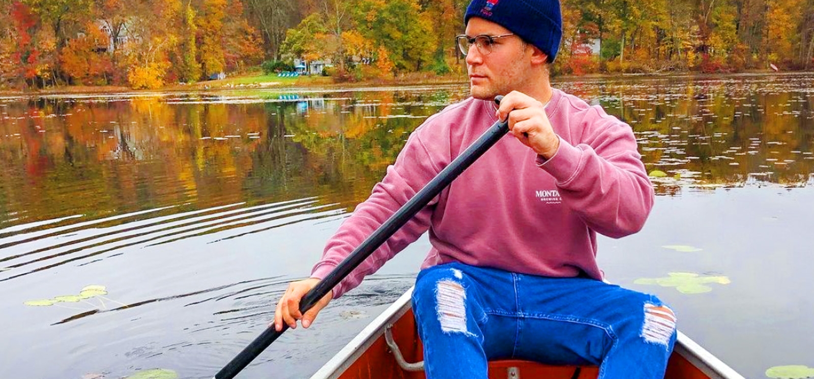 Un hombre con un suéter rosa rema en una canoa a través de un estanque tranquilo.