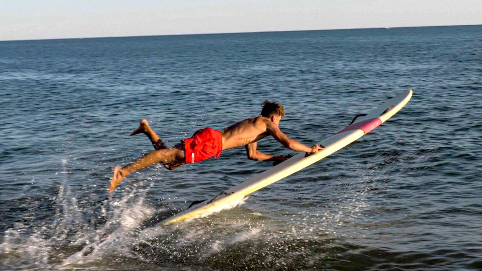 Lifeguard jumping onto longboard to save swimmer