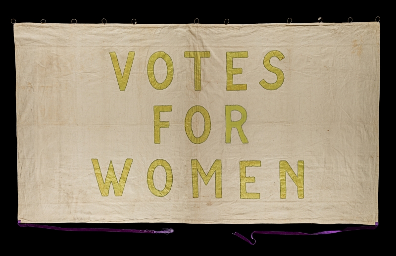Banner with yellow text reading "Votes for Women"
