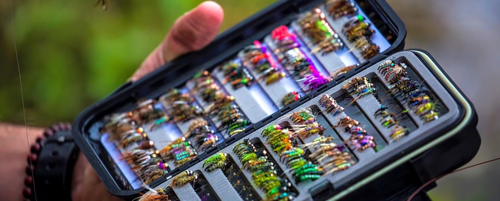 Hombre sujetando un kit de pesca con mosca lleno de lazos para moscas