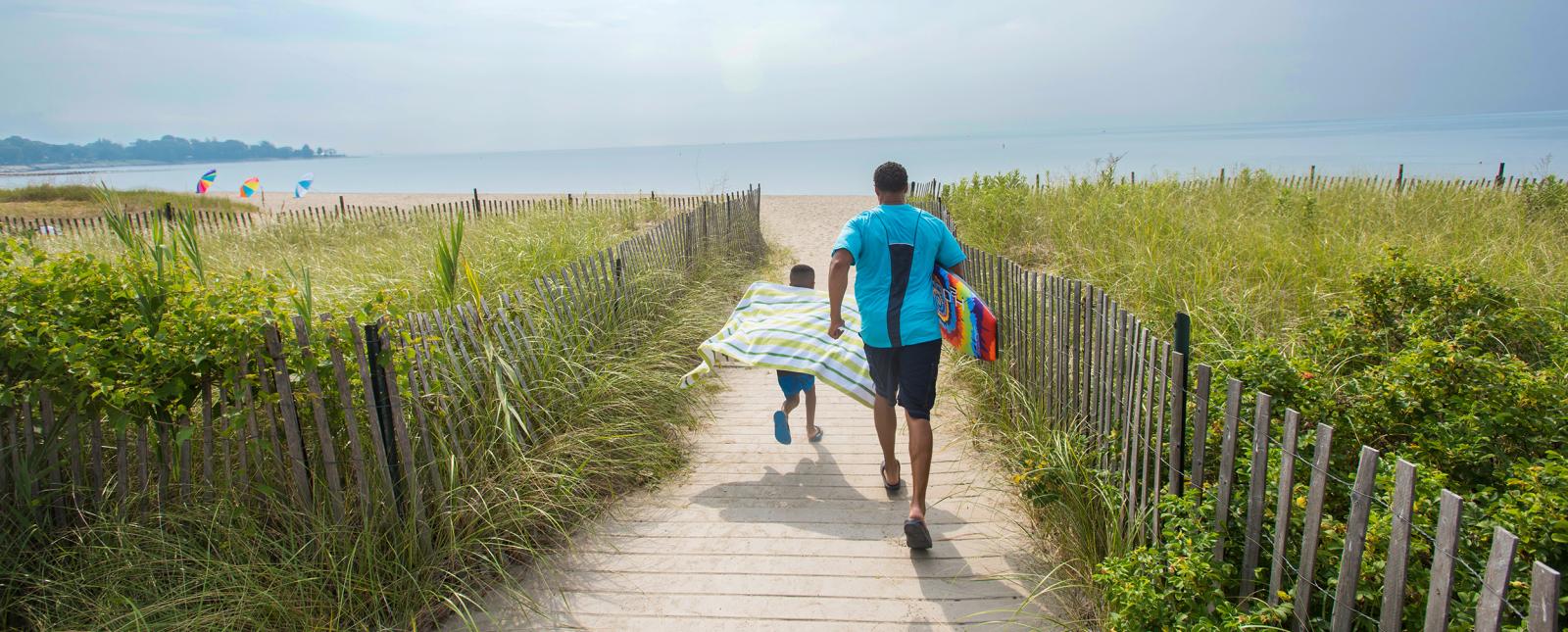 Padre e hijo corriendo por el camino hacia la playa en Sherwood Island State Park