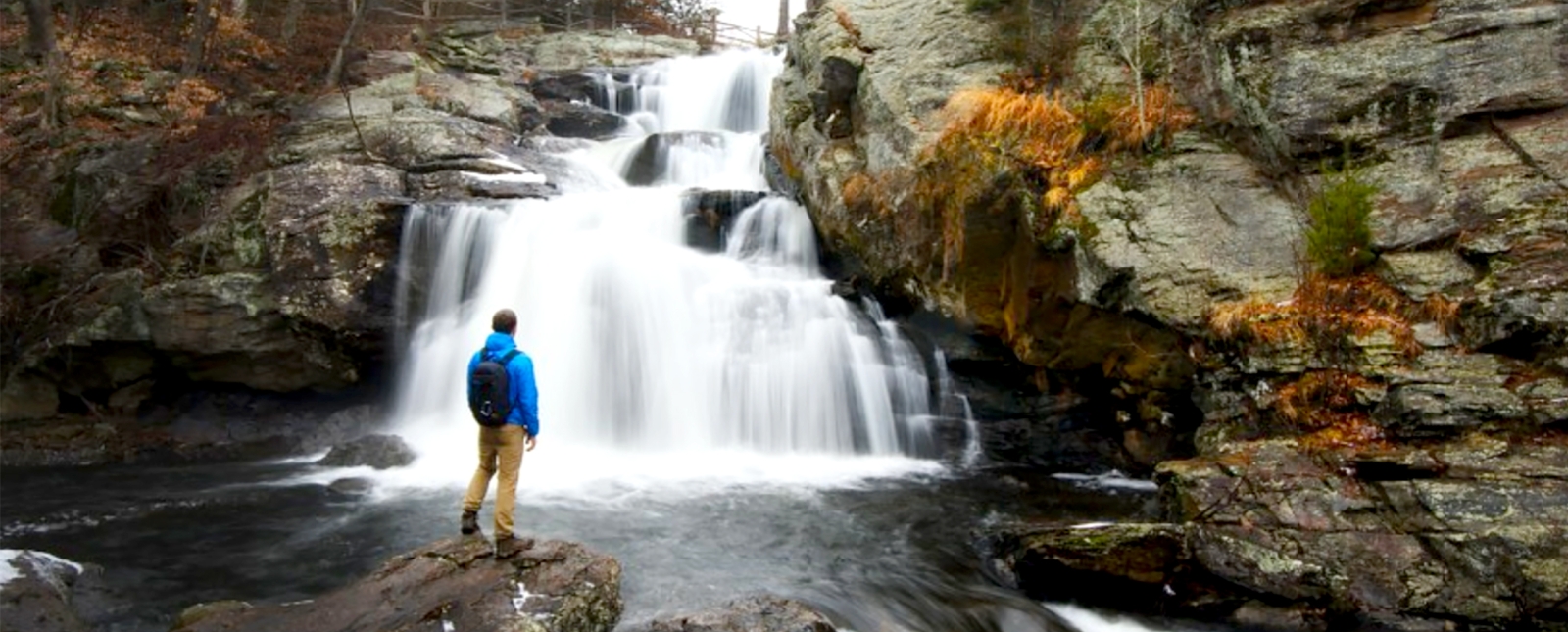 Caminante de pie sobre las rocas mirando la cascada en el Parque Estatal Devil's Hopyard (Instagram@smithfarmgetaway)