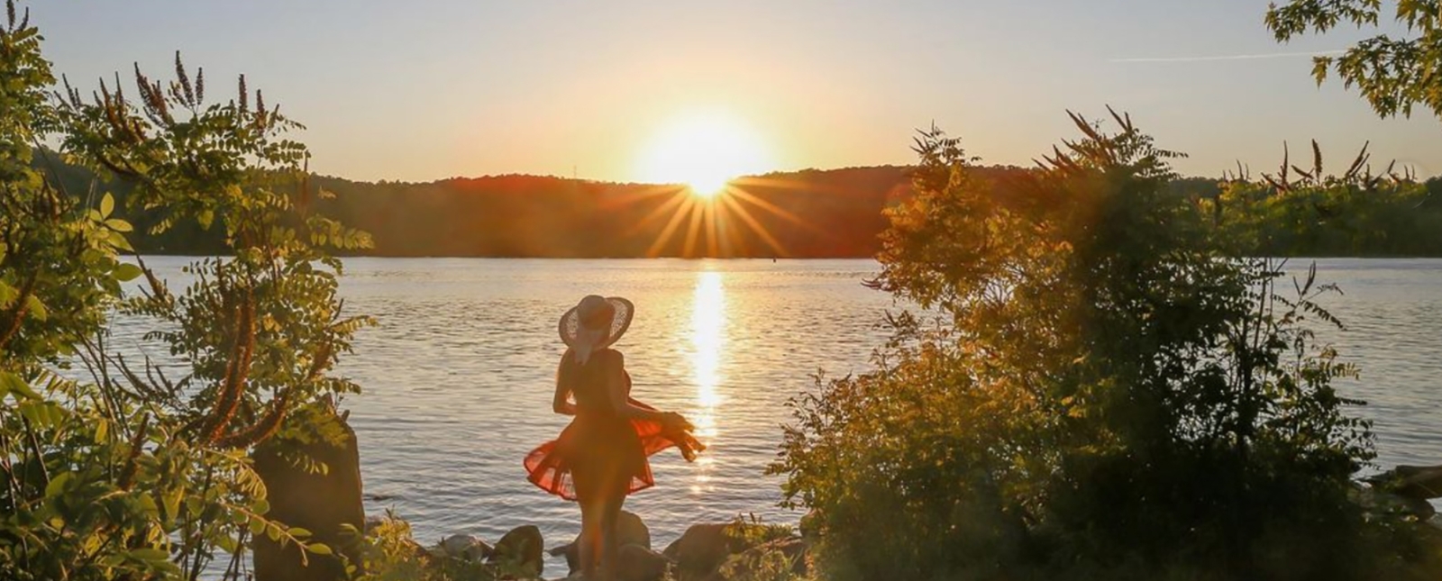 Una mujer de pie sobre las rocas mirando la puesta de sol sobre el agua (Instagram@fotolga_)