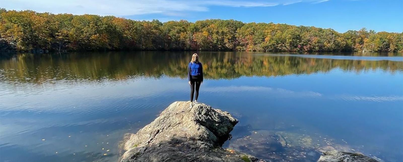 a woman standing on a rock in front of water reflecting trees and sky (Instagram@lenahrystyk)