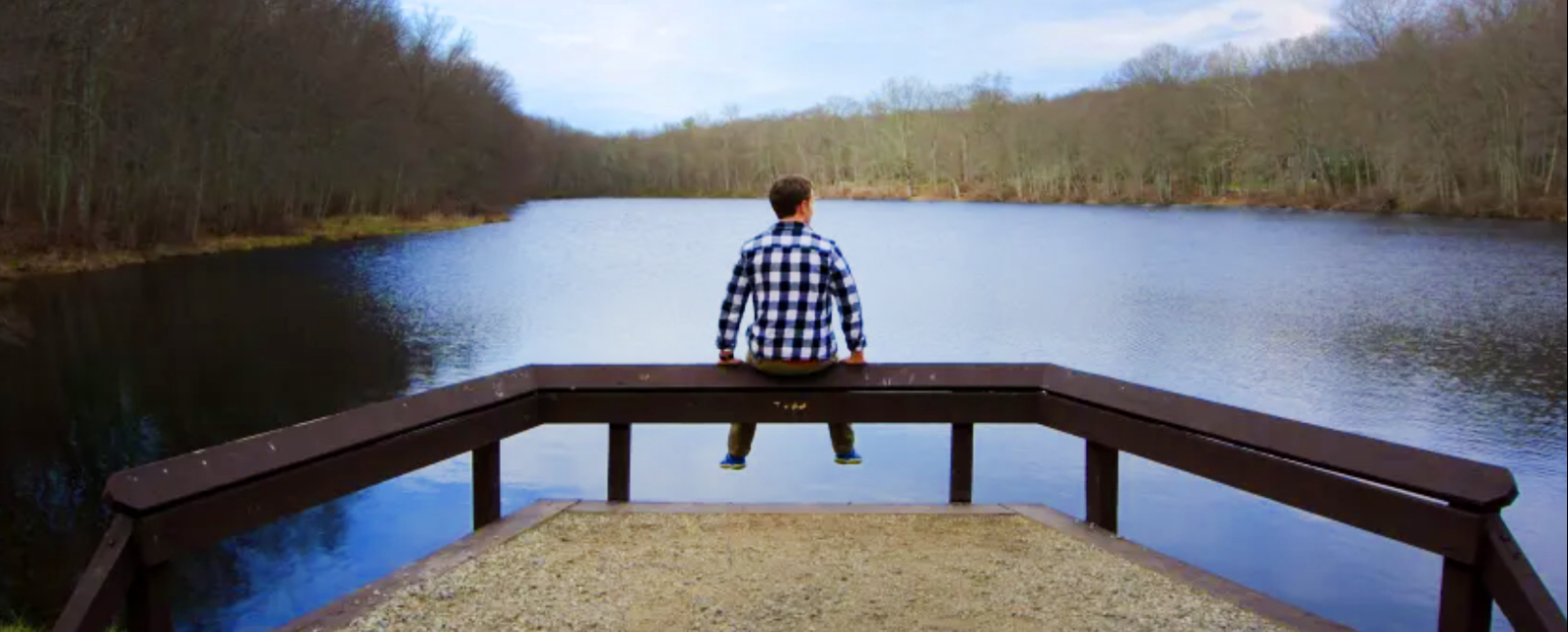 A man sitting on the railing of a dock overlooking water.