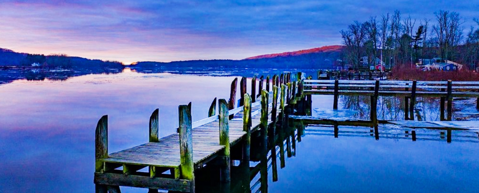 Un muelle sereno al atardecer, enmarcado por un cielo azul y un entorno invernal.