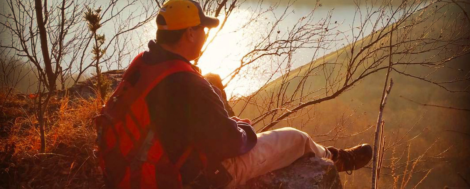 Un hombre sentado sobre una roca al atardecer, contemplando la naturaleza.
