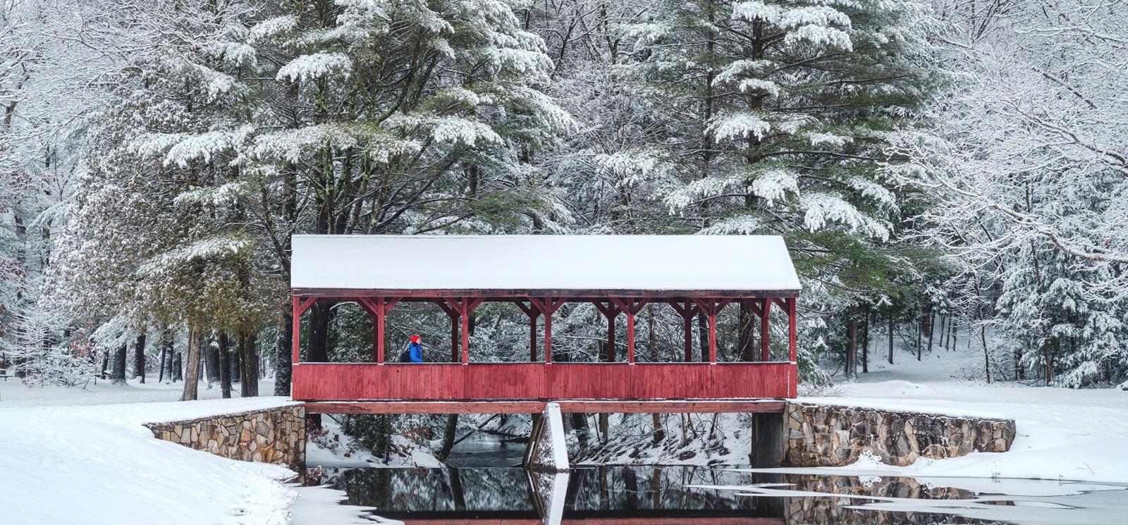 Winter scene of woman on covered bridge at Stratton Brook State Park