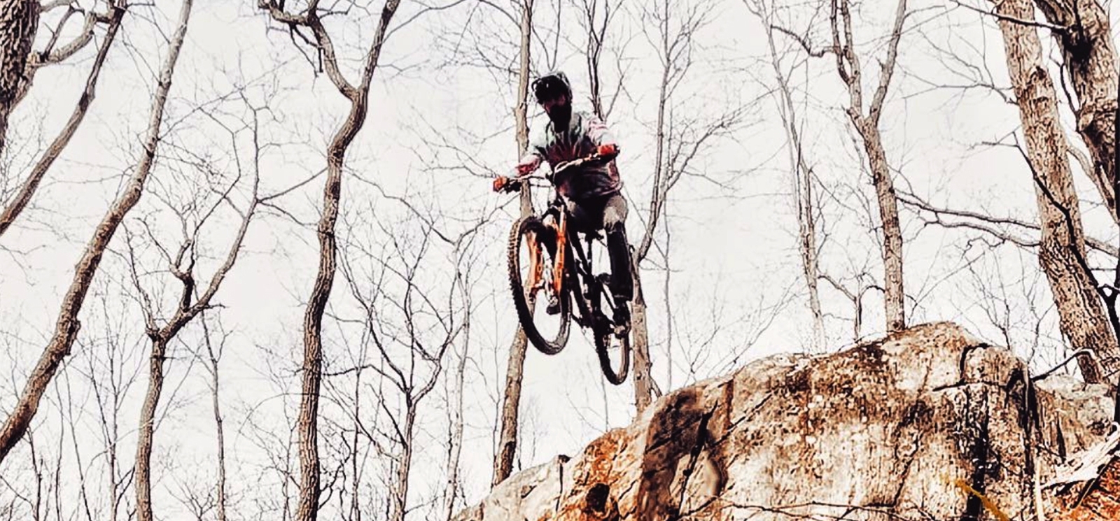 A man going over a jump on a mountain bike in the woods (Instagram@weycyde)