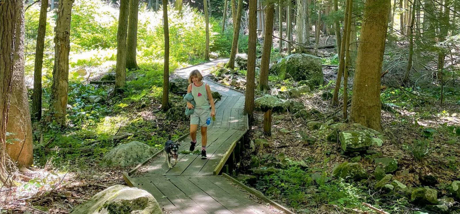 A woman hiking with her dog on a path through the woods (Instagram@mommawanderer)