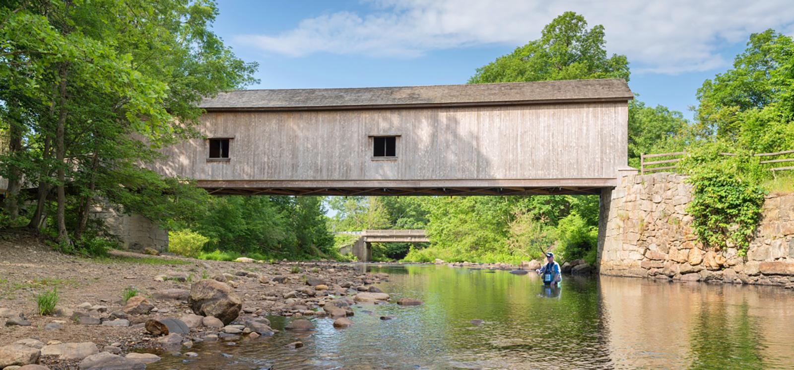 A fisherman in the water under a covered bridge (CTVisit)
