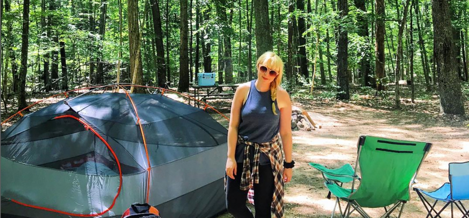 A woman standing at campsite in the woods (Instagram@carriwiniker)