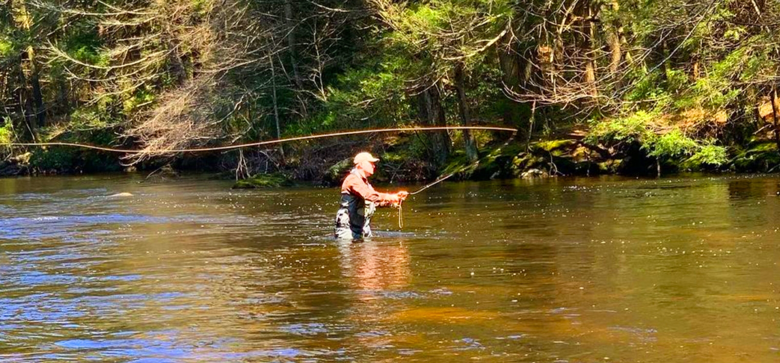  Un hombre pescando en un río con una caña de pescar.
