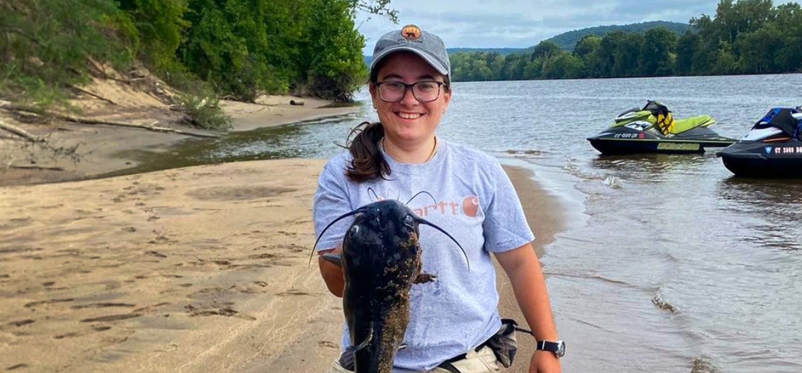 A person on a sandy beach happily holds a fish they caught.