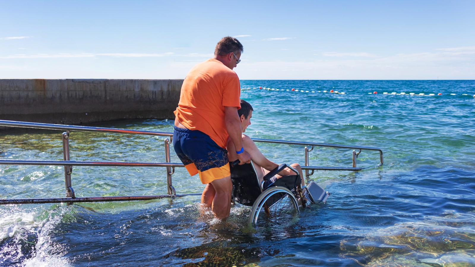 Hombre empujando a un amigo por una rampa de agua accesible para sillas de ruedas
