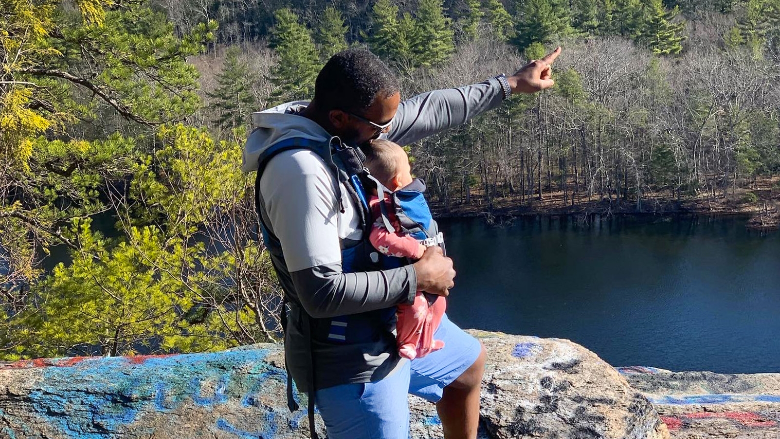 A man holding a baby on an overlook above water.