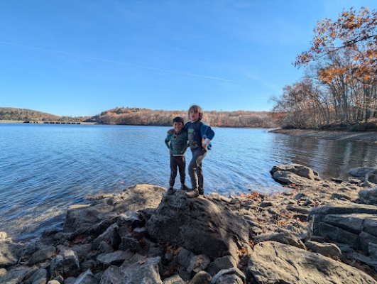 two children standing on rocks in front of water at paugussett