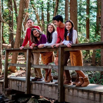 A family standing on a small wood bridge over a stream (Instagram@taylorwaltonphoto)