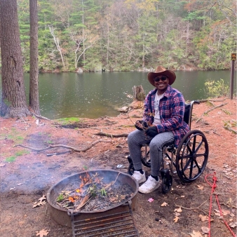 Un hombre en silla de ruedas junto a un incendio en un camping en el bosque (Instagram@breslifexo)