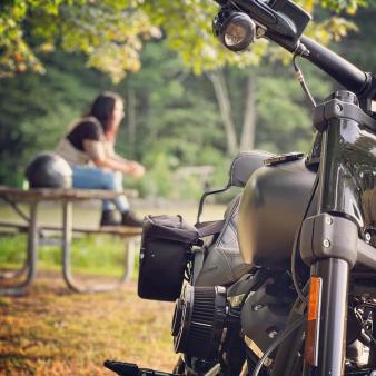 Un motociclista sentado en un banco del parque con una motocicleta estacionada en primer plano (Instagram@ladybeast_fit)