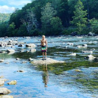 Un niño parado sobre las rocas de un río (Instagram@malinda_ferko)