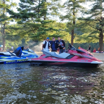 Men pose for a picture by waterside with jet skis