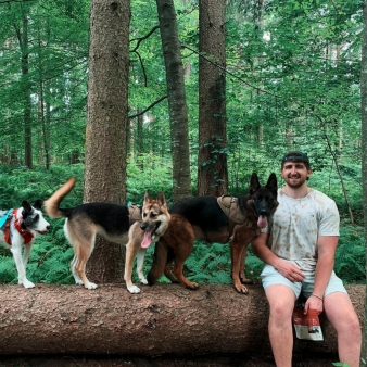 A man with three dogs sitting on a fallen tree in the woods (Instagram@maximilianbhansen)