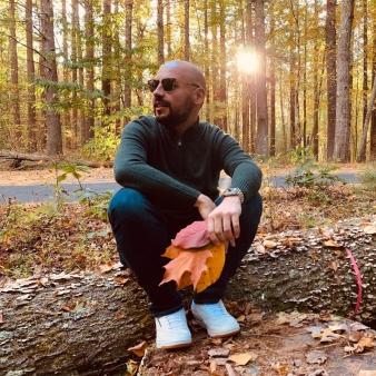 A man poses on a log holding leaves in the woods (Instagram@jonathan_antonio16)