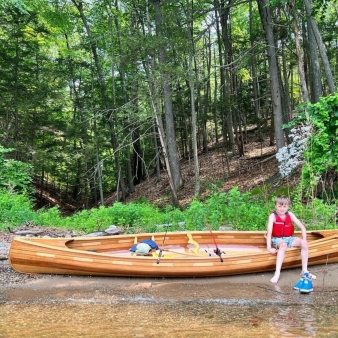 A boy sits in a wooden canoe on the shore of the lake (Instagram@seankeenan)