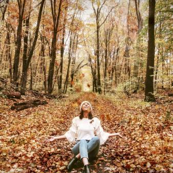 A woman sits on a path in the woods that is covered with autumn leaves (Instagram@jess.k.thibault)