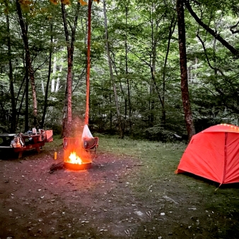 A tent and picnic table near a camp fire in the woods (Instagram@subway_churros)