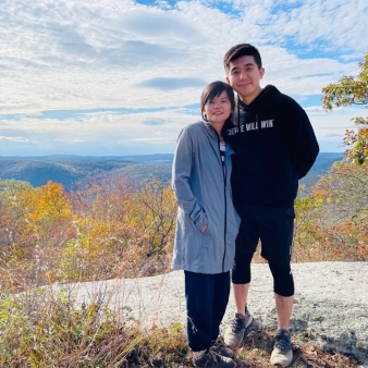 A couple poses for a photo overlooking a view of fall trees (Instagram@roxanneechenwh)