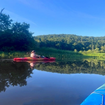 Una mujer navegando en kayak en aguas tranquilas que reflejan los árboles y el cielo (Instagram@jskwrite)