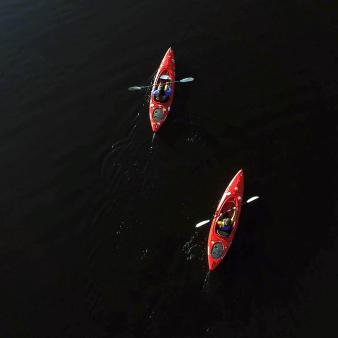 An aerial view of two people kayaking on dark water
