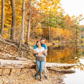 Una pareja apoyada en un tronco cerca del lago con árboles de otoño al fondo (Instagram@mollymiaphotography)