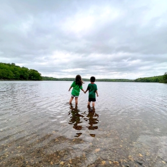 Dos niños tomados de la mano chapoteando en el agua del lago (Instagram@loconnecticut)