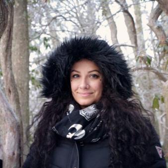A woman with black fuzzy hat poses in front of winter trees (Instagram@trinaembers)