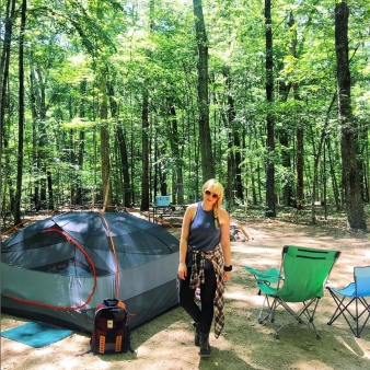 A woman standing at campsite in the woods (Instagram@carriwiniker)