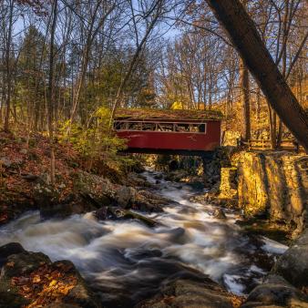 A red covered bridge over a river in the woods (Flickr@Lechmoore-Simms)