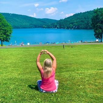 Woman on green in front of Squantz Pond making heart sign (Instagram@drica_viajante)