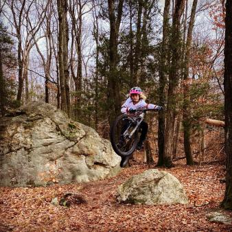 A woman mountain biking in the woods (Instagram@brooksinct)