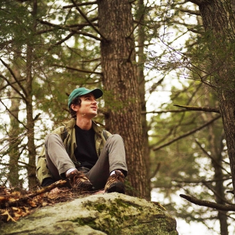 Un hombre disfrutando de la naturaleza, sentado sobre una roca en el tranquilo bosque.