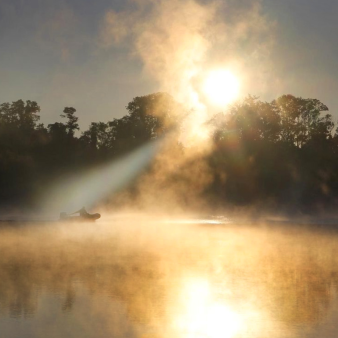 Un barco se desliza sobre el agua mientras el sol atraviesa la niebla en el Parque Estatal River Highlands.
