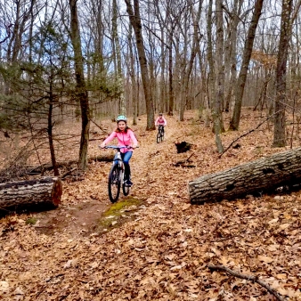 Dos niñas explorando un sendero forestal en bicicleta.