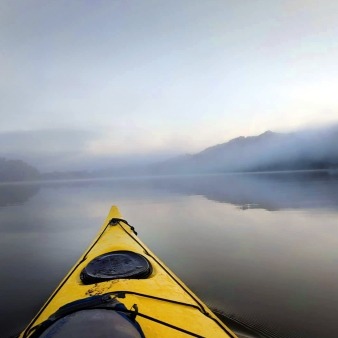 Un río sereno con un kayak deslizándose por aguas tranquilas, rodeado de una niebla brumosa.