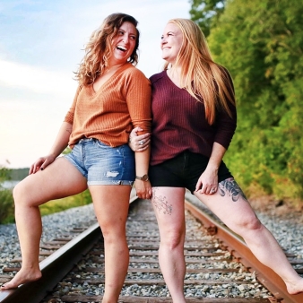 Two women smiling at eachother posed on the railroad tracks at Stoddard Hill State Park