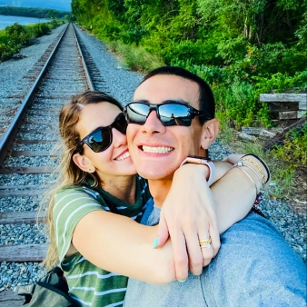 Una pareja sonriente abrazándose en una vía de tren.